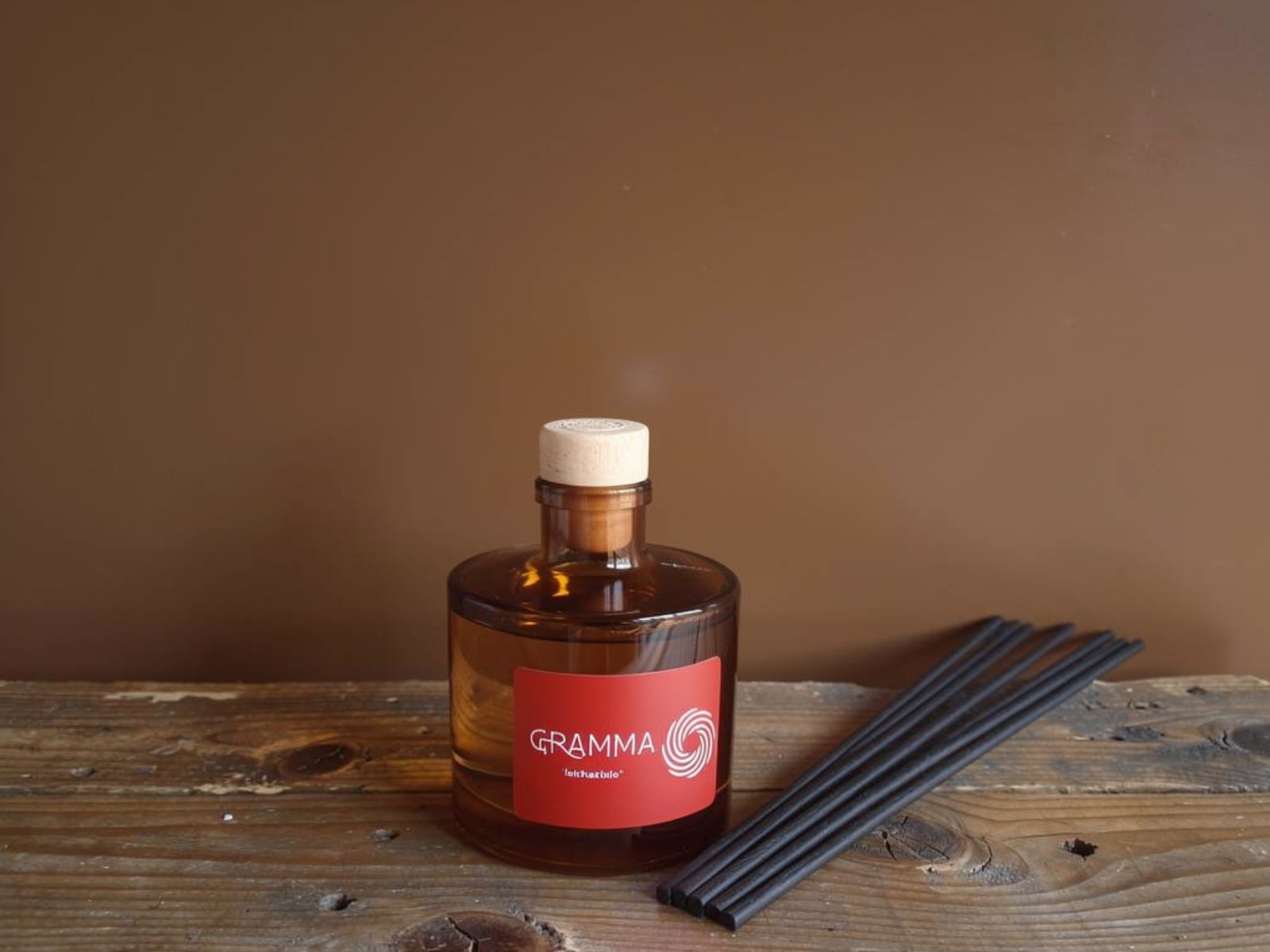 Ένα κομψό γυάλινο αρωματικό χώρου (reed diffuser) της GRAMMA, ακουμπισμένο πάνω σε μια παλαιωμένη ξύλινη επιφάνεια. Στην κόκκινη ετικέτα διακρίνεται το λογότυπο του λαβύρινθου. Δίπλα στο μπουκάλι βρίσκονται τακτοποιημένα μαύρα στικς διάχυσης. Το φόντο είναι σε μια ζεστή, γήινη καφέ απόχρωση, αποπνέοντας απόλυτη ηρεμία και την αίσθηση του Ησυχαστηρίου.