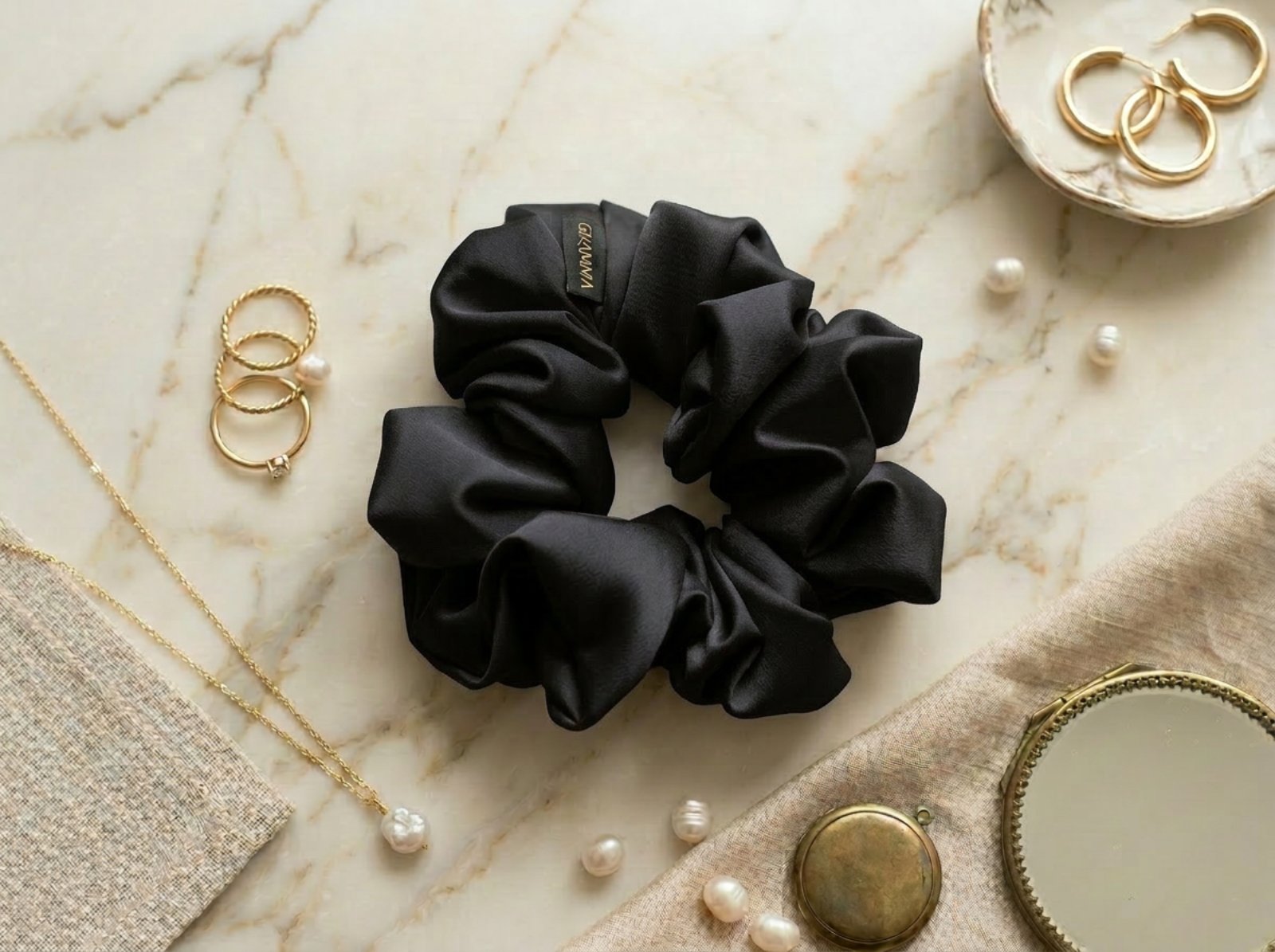 Collection of handmade satin GRAMMA scrunchies in various colors and patterns (Zebra Print, Ochre). Featured in hair styling, close-up with the brand label, and flat lay compositions with jewelry on wooden and marble surfaces.