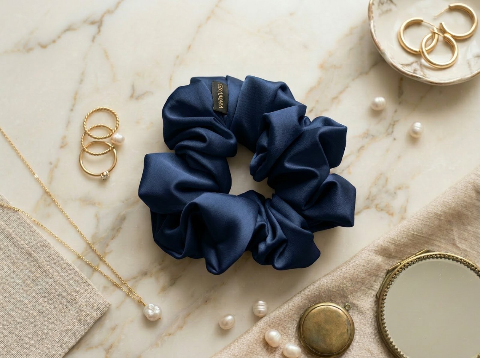 Collection of handmade satin GRAMMA scrunchies in various colors and patterns (Zebra Print, Ochre). Featured in hair styling, close-up with the brand label, and flat lay compositions with jewelry on wooden and marble surfaces.