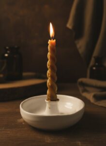 Handmade white ceramic candle holder by GRAMMA featuring a lit twisted beeswax candle on a wooden surface with warm, atmospheric lighting.